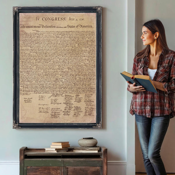A woman stands in a room, holding a book and looking at a framed document hanging on the wall.