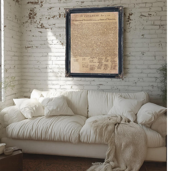 a white couch with a framed document hanging above it on a white brick wall.